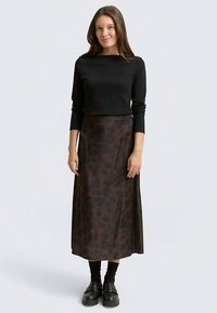 Haut noir à manches longues associé à une jupe longue imprimé léopard marron. La tenue présente une coupe slim et est complétée par des bottines noires épaisses.