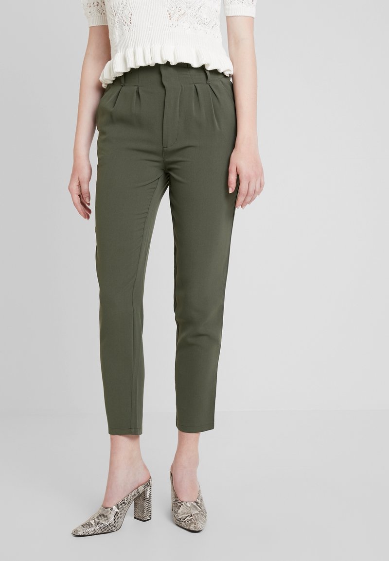 Pantalon ajusté vert olive avec pinces à l'avant, associé à un haut en tricot léger et des mules à talons imprimé serpent, avec un design de talon bloc.