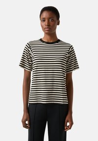 Koszulka w paski z czarnymi i kremowymi poziomymi paskami, krótkimi rękawami i okrągłym dekoltem, zestawiona z czarnymi, dopasowanymi spodniami.