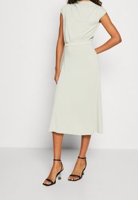 Ljusgrön knälång klänning med korta ärmar, samlad midja och mjuk struktur. Kombinerad med svarta, remmar pumps för kontrast.