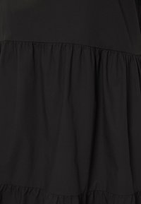 Schwarzes Kleid mit einem strukturierten Oberteil und gestuftem Rock. Der Stoff ist glatt und weist an den Nähten Raffung auf, um zusätzliches Volumen zu erzeugen.