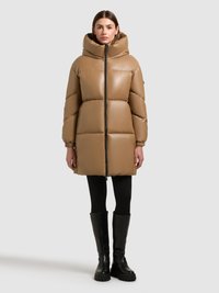 Puhasta jakna v bež barvi z visokim ovratnikom, zadrgo in sproščenim krojem. Ima rebraste manšete in stranske žepe, oblečeno z črnimi škornji do kolen.