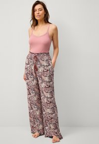 Lichtroze geribbelde tanktop gecombineerd met losse, gemusterde broek met een bloemmotief in bordeauxrood, crème en zwart.