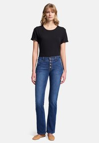 Jeans in denim blu con vita alta, chiusura a cinque bottoni e gamba bootcut. Abbinati a una maglietta nera aderente. Scarpe beige piatte completano il look.