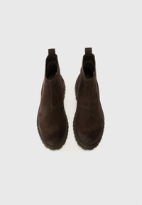 Botas de tobillo de ante marrón con una parte superior texturizada, paneles laterales elásticos y una suela resistente para mayor agarre. Diseño minimalista y detalles de costura.