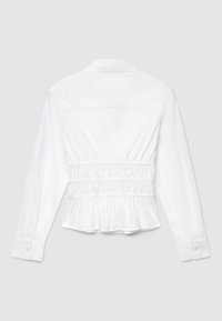 White long-sleeve shirt featuring a cinched waist, peplum hem, button cuffs, and a collar. Smooth fabric with a plain texture.