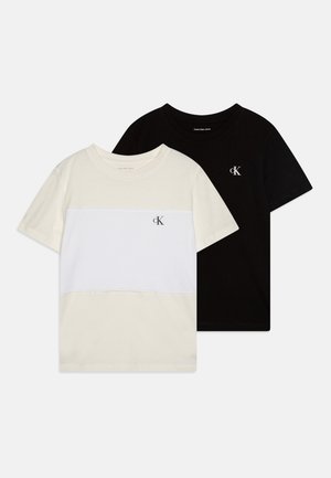 Duos marškinėlių: vieni kreminiai su baltu horizontaliu dryžiu, o kiti visiškai juodi, abu pagaminti iš medvilnės, su Calvin Klein logotipu.