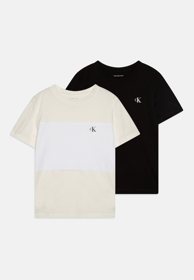 Twee t-shirts: een crème kleurige met een witte horizontale streep en de andere volledig zwart, beide gemaakt van katoen, met het Calvin Klein logo.