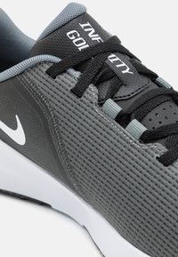 Pantofii atletici gri cu partea superioară din plasă, șireturi negre și un logo alb în formă de swoosh. Dispun de o limbă căptușită și un material texturat pentru aderență.