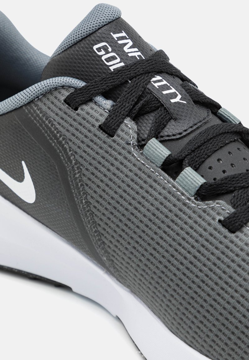 Grauer Sportschuh mit Obermaterial aus Mesh, schwarzen Schnürsenkeln und einem weißen Swoosh-Logo. Verfügt über eine gepolsterte Zunge und eine strukturierte Oberfläche für besseren Halt.