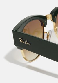 Roheline plastist prillid, millel on pruunid gradueeritud objektiivid, nurgeline disain ja kullatud Ray-Ban logo küljel. Detailid hinge aktsentides.