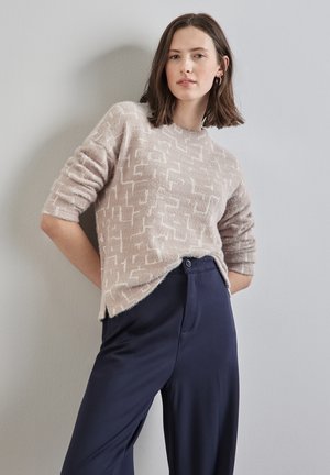 Helles rosa Sweatshirt mit einem strukturierten geometrischen Muster, Rundhalsausschnitt und Dreiviertelärmeln, kombiniert mit dunkelblauen Hosen.
