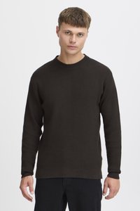 Dark brown knitted sweater with a textured finish, round neckline, and long sleeves, paired with black pants.