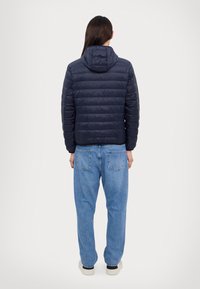 Doudoune navy avec un motif de matelassage horizontal, capuche, poignets élastiques et ourlet ; associée à un jean bleu clair à coupe ample.