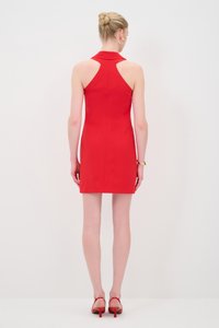 Abito rosso senza maniche con colletto alto, design aderente e dettagli a scollo. Il modello indossa tacchi rossi abbinati, mostrando gambe scoperte.