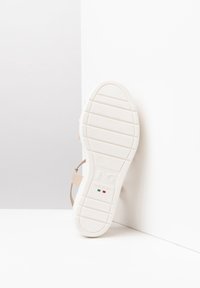 Sandalo con suola bianca e cinturino beige, caratterizzato da una texture liscia e un design minimalista. Presenta marchi del brand e etichetta "made in Italy".