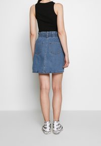 Jeanskjol med resår i midjan, blå färg, två bakfickor, bärs med en svart ärmlös topp och vita sneakers med grafik.