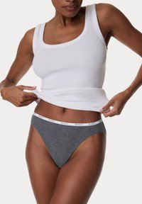 Graue Strings mit einem weißen elastischen Bund, auf dem das Wort "BODY" steht. Das Model trägt ein enges, weißes Rippentop.