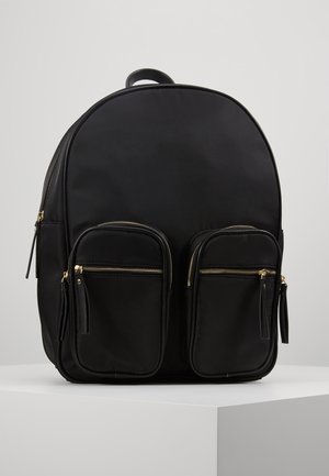 Zwarte rugzak met afgeronde bovenkant, twee voorzakken met rits en tassel-ritstrekker, en een handvat bovenop, weergegeven op een witte ondergrond.