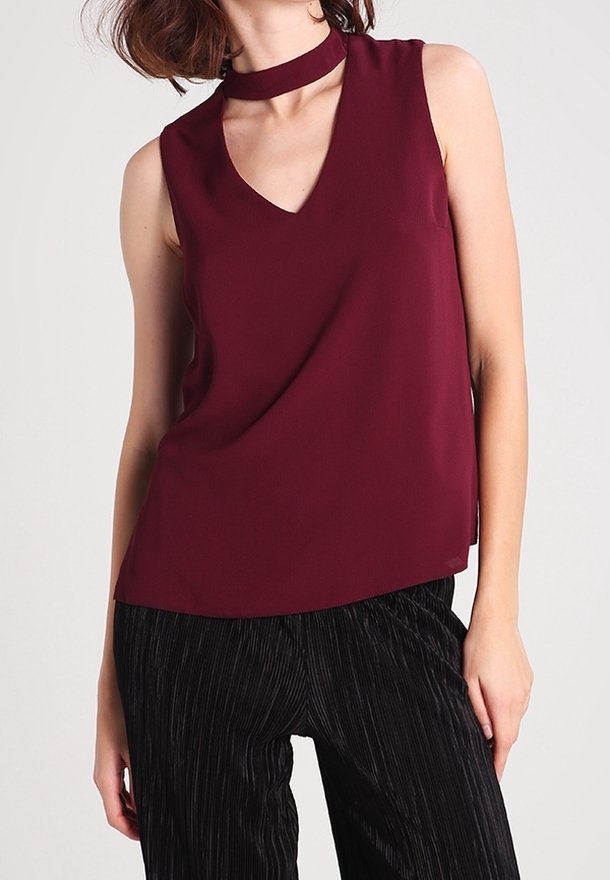 Burgundy ärmlös topp med V-ringning och choker-detalj, gjord av ett glatt tyg, kombinerad med svarta byxor med smala ränder.