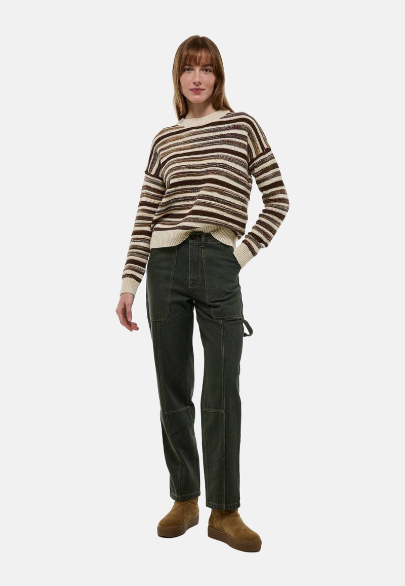 Pull rayé en crème, marron et rouille ; associé à un pantalon cargo vert olive avec poches latérales ; le modèle porte des bottes en cuir suédé marron.