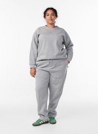 Ensemble sweat-shirt et pantalon de survêtement gris en tissu doux. Le haut présente un col rond et le pantalon une taille à cordon, assortis à des baskets vertes.