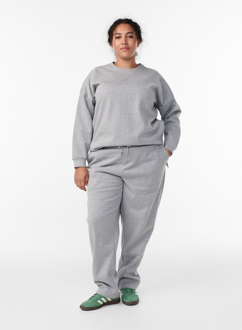 Ensemble sweat-shirt et pantalon de survêtement gris en tissu doux. Le haut présente un col rond et le pantalon une taille à cordon, assortis à des baskets vertes.