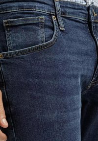 Granatowe dżinsy z klasycznym pięciopocketowym fasonem, widocznymi szwami i delikatnym wytarciem materiału.