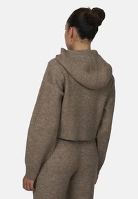 Przycięty, brązowy sweter z kapturem wykonany z miękkiej dzianiny. Posiada ściągacze na rękawach i u dołu oraz luźny krój i teksturowaną powierzchnię.