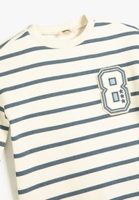 Felpa a righe in crema e blu navy, con scollatura rotonda, maniche lunghe e un patch ricamato con la cifra "8" e stelle sul petto.