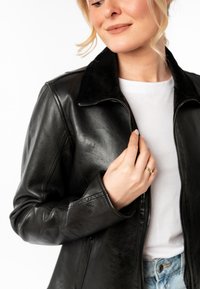 Zwart leren jack met een suède kraag, voorkant met rits en een getailleerd ontwerp. Draag het over een wit shirt en spijkerbroek, waarmee de soepele textuur wordt getoond.