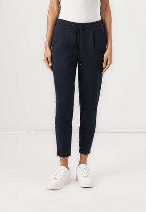 Marine joggers met een trekkoord in de taille, taps toelopende pijpen en zakken, gemaakt van een zachte stof, gecombineerd met witte sneakers.