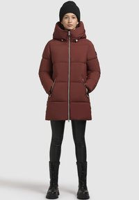 Bordeaux pufferjakke med høj krave, lynlås lukning og to sidelommer; båret med sorte leggings og knæhøje snørebåndsstøvler.