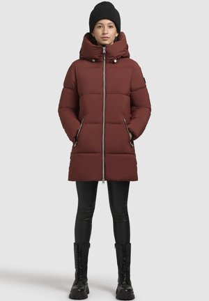 Abrigo acolchado burdeos con cuello alto, cierre de cremallera y dos bolsillos laterales; llevado con leggins negros y botas de caña alta con cordones.
