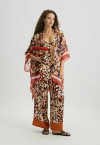 Leopardprint kimono en bijpassende wijde broek van doorschijnende stof, met rode accenten en een bijpassende clutch.