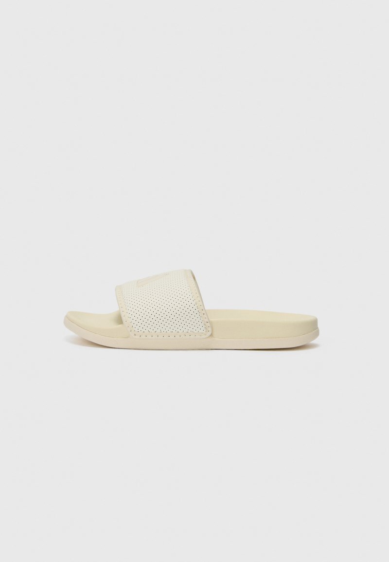 Light beige slide sandals with a textured upper featuring small perforations, a flat sole, and smooth edges for comfort.