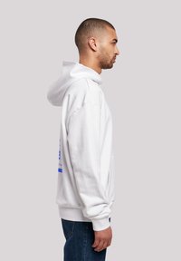 White hoodie with a hood, featuring a front pouch pocket and blue graphic print. Paired with dark blue jeans. Smooth fabric texture.