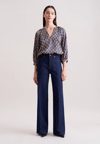 Blouse met patroon en V-hals, driekwart mouwen, en donkerblauwe wijde jeans met een klassieke denimstructuur.