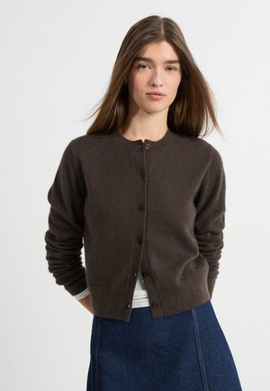 Brauner Woll-Cardigan mit rundem Halsausschnitt, langen Ärmeln und Knopfverschluss. Die weiche Textur und der figurbetonte Schnitt ergänzen einen Jeansrock.
