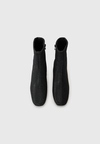 Black ankle boots with a slim, smooth design, featuring a zip closure. The material has a subtle shimmer and a textured finish.