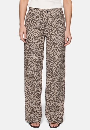 Femme portant un pantalon à jambes larges avec un imprimé léopard beige et marron, associé à des sandales noires à bout ouvert et un haut blanc.