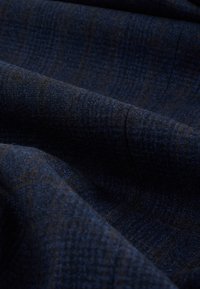 Tissu bleu foncé avec un motif à carreaux subtil et de légers plis créant des ombres douces et de la texture.