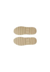 Suole delle scarpe color crema con una superficie texturizzata, caratterizzate da scanalature orizzontali e un emblema rettangolare al centro.