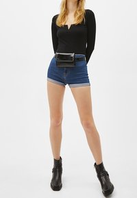 Maglietta nera a maniche lunghe, shorts di jeans a vita alta con risvolti, borsa a cintura nera e stivaletti neri con tacco largo e dettagli con fibbia.