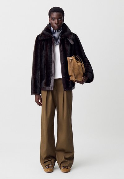 Chaqueta de piel sintética con una paleta de colores marrón y negro, parte superior crema, pantalones anchos marrones y un bolso de ante color arena. Una bufanda de rayas añade detalle.