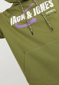 Felpa verde oliva con un ampio grafico bianco e viola, cordini regolabili con un motivo a righe e una tasca marsupiale anteriore.