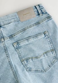 Svijetloplavi traperice s stražnjim džepom, vidljivim šavovima i sivoj kožnoj etiketom s natpisom "DENIM SUPPLY."