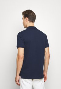 Navy blue polo shirt in cotton with short sleeves, ribbed collar, and side slits at the hem. Plain design with no visible patterns.