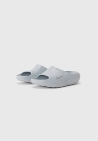 Svijetlosive klizne sandale s teksturiranim gornjim dijelom, otvorenom prstohvatom i bočnim izrezima. Imaju srebrni Nike logo i rebrasti potplat za prianjanje.