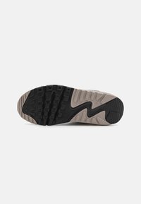 Nike tenisica s potplatom s crnim uzorkom gume, bež srednjim dijelom, teksturiranom površinom i valovitim dizajnom. Sadrži uzdignute dijelove za bolji rukohvat.
